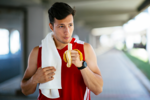 a muscular man wearing sports clothes and eating a banana 