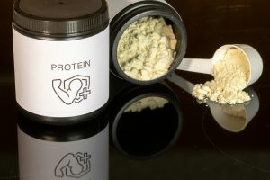 A tub of protein powder labelled "Protein" with an illustration of muscles and protein scoop often used by athletes