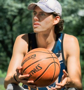 Basketball player sitting down with a basketball in his hand on a sunny day